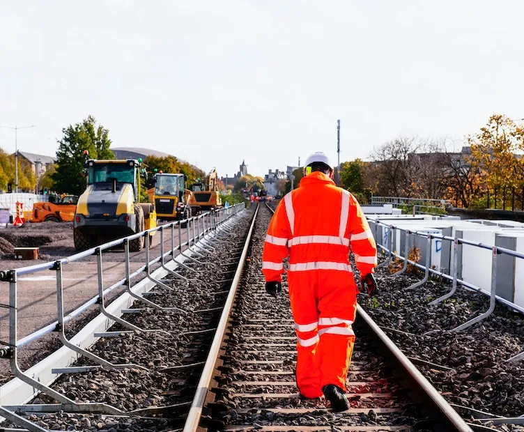Rail technician in hi-vis PPE walking along the train tracks